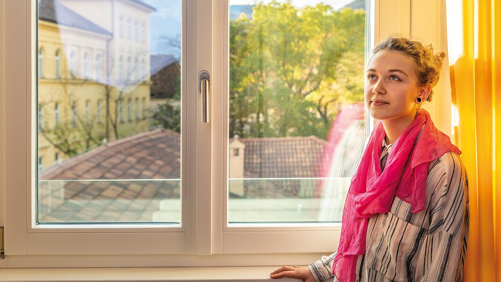 Una ragazza siede accanto alla finestra nello studentato a Bolzano per ragazze