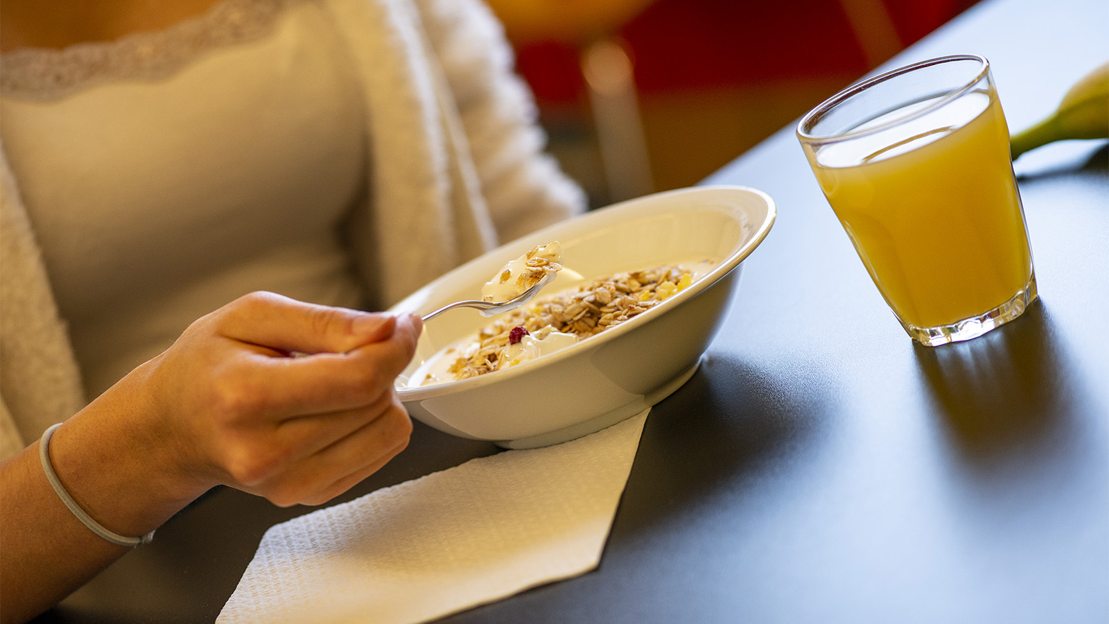 eine Schüssel Müsli mit Joghurt und ein frischer Fruchtsaft werden von einem Mädchen in Mädchenheim zum Frühstück gegessen