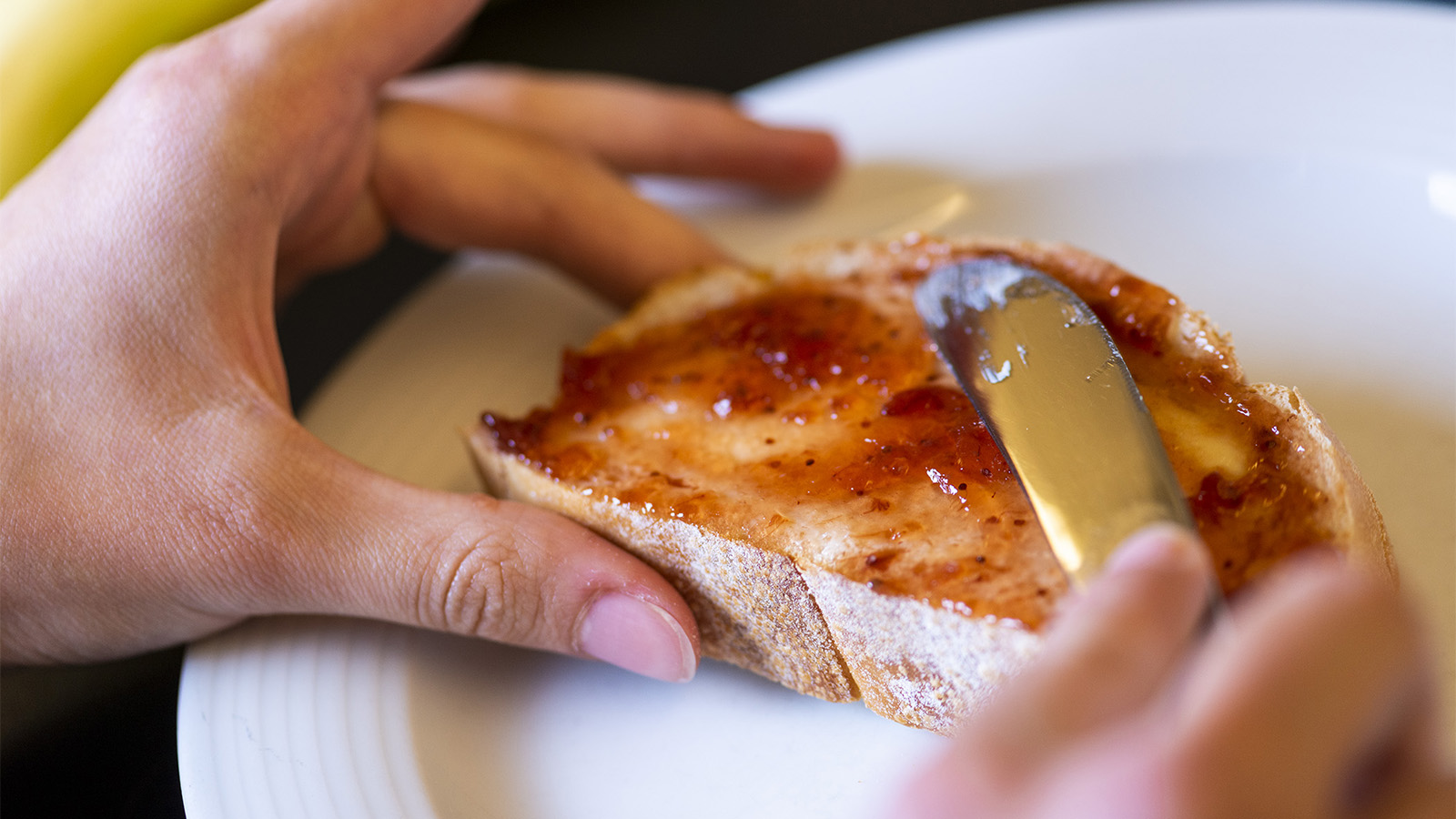Detailaufnahme einer Mädchenhand die mit dem Messer Marmelade auf ein Brot streicht